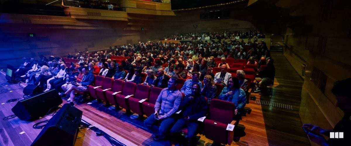 A large audience fills the red-seated auditorium of a concert hall during a performance evening.