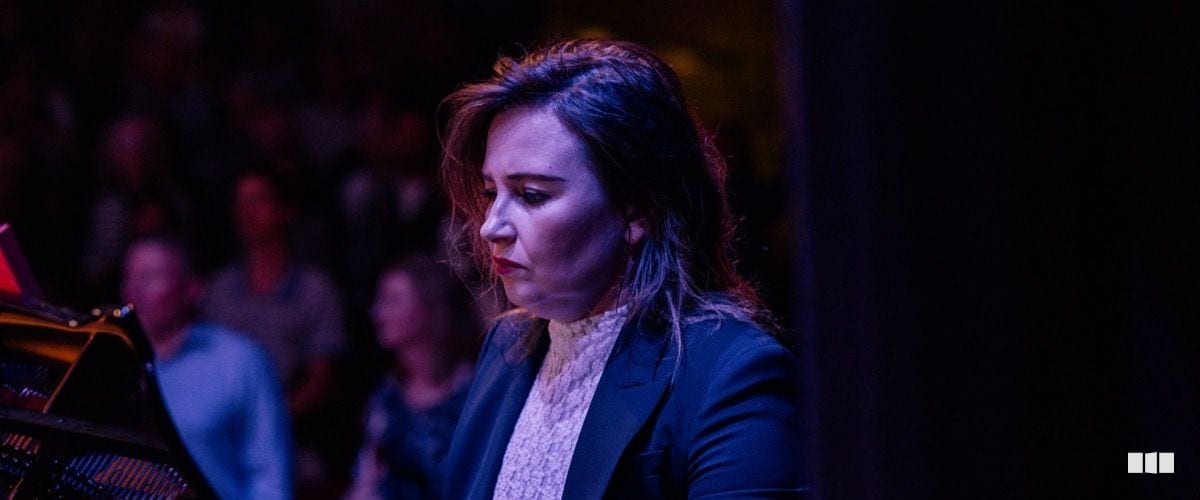 A female pianist performs with focused concentration at a grand piano before a concert audience