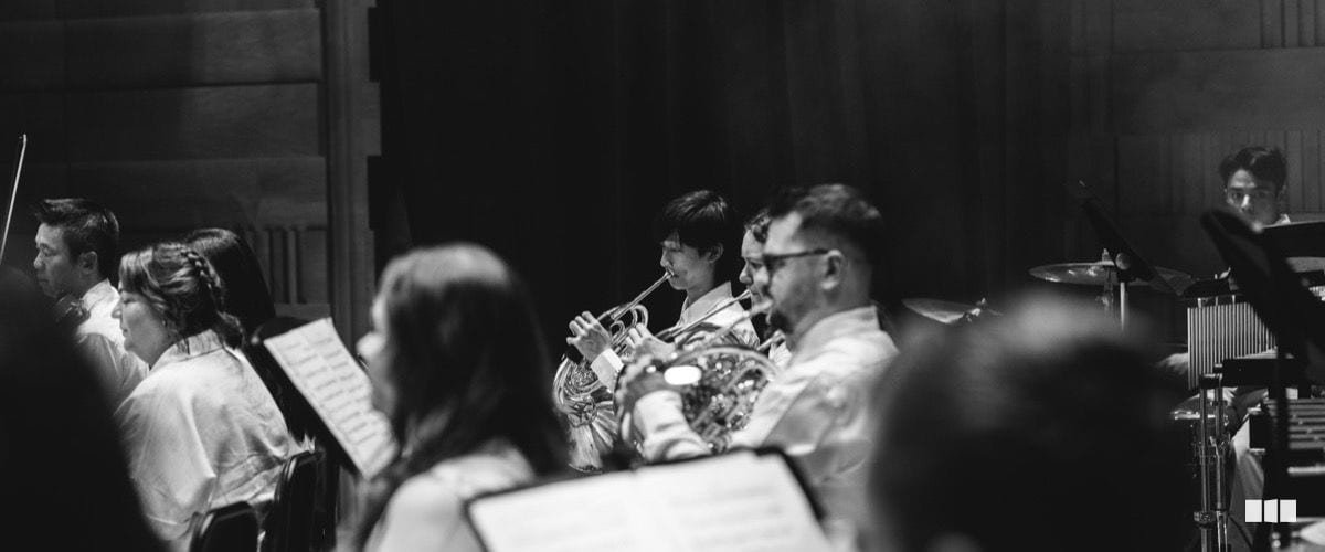 Brass players perform from sheet music during an orchestral rehearsal or concert in a darkened hall