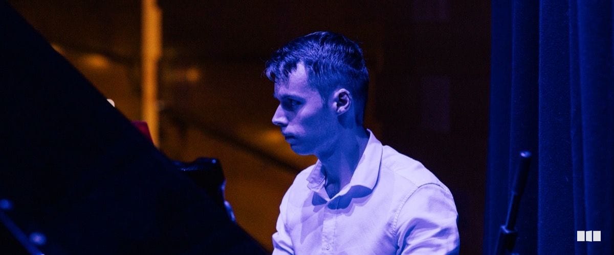 A young male pianist performs under dramatic blue stage lighting at a concert.