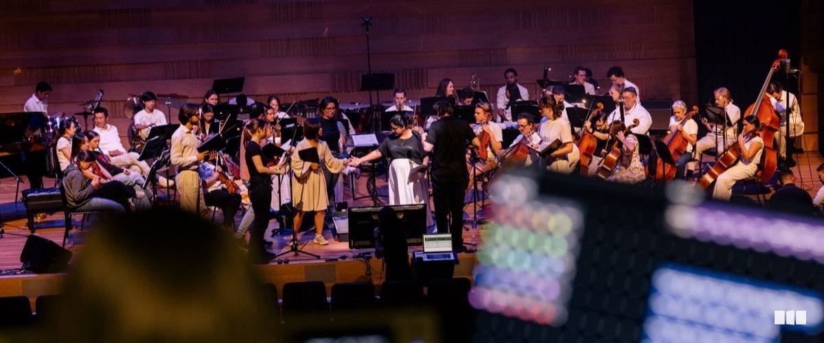 Orchestra musicians on stage take a bow with the conductor after a performance in a concert hall