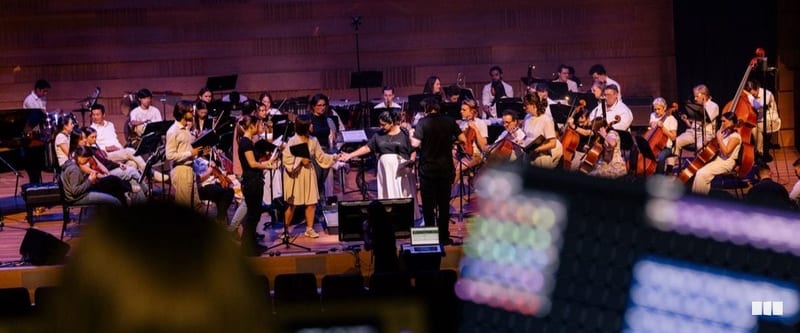 Orchestra musicians on stage take a bow with the conductor after a performance in a concert hall