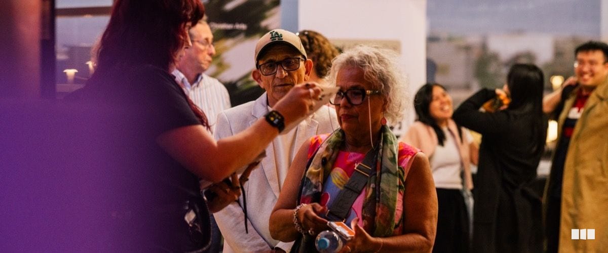 A diverse group of attendees mingle and converse at what appears to be an arts event reception or foyer gathering.