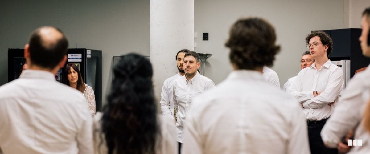 A group of musicians in white shirts stand in a circle during what appears to be a pre-concert gathering or briefing backstage.