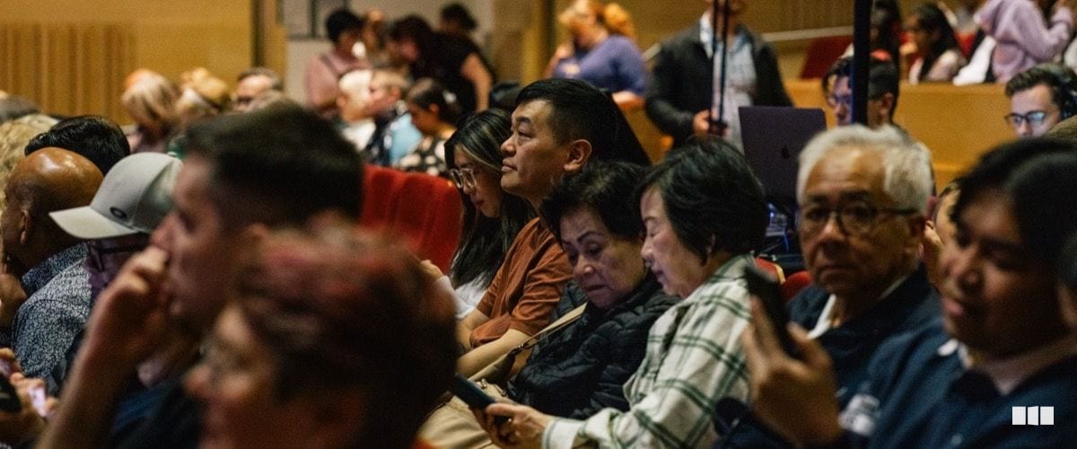 A diverse audience seated in an auditorium attentively watches a performance