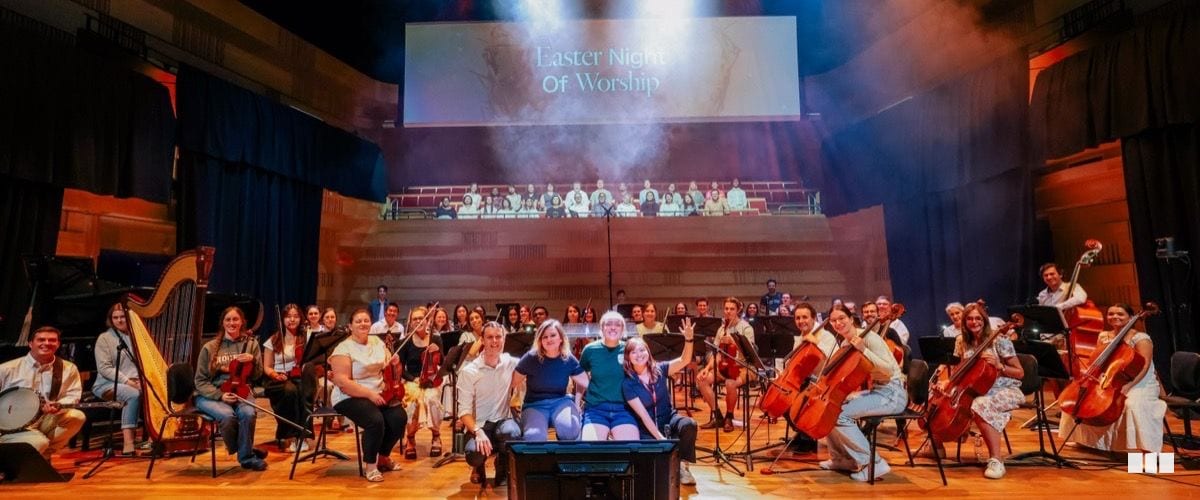The full orchestra and choir gather on stage for a group photo at the Easter Night of Worship event in a concert hall