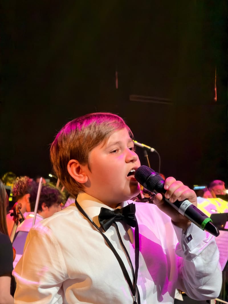 A youth vocalist performing under stage lights at the Australian Christian Proms.